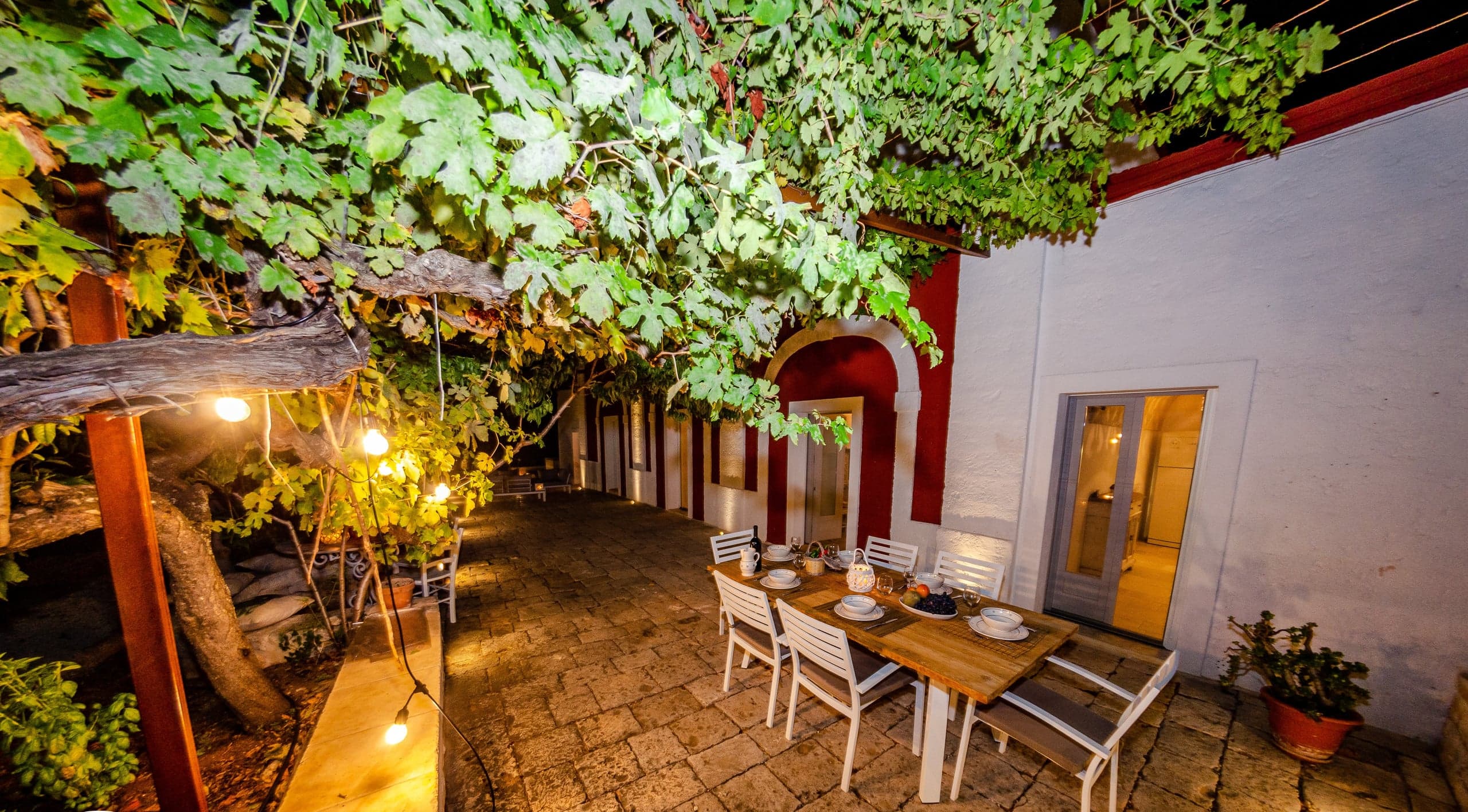 The dinner table set on the terrace at dusk, under the string lights
